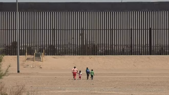 Một phụ nữ và ba trẻ nhỏ chạy đua về phía bức tường ở biên giới Mỹ - Mexico ở Ciudad Juárez, Mexico.
