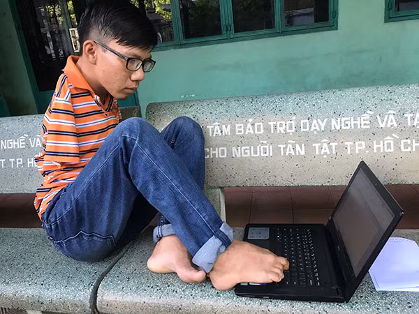 Trần Dương đang dùng ngón chân đánh văn bản trên máy tính.