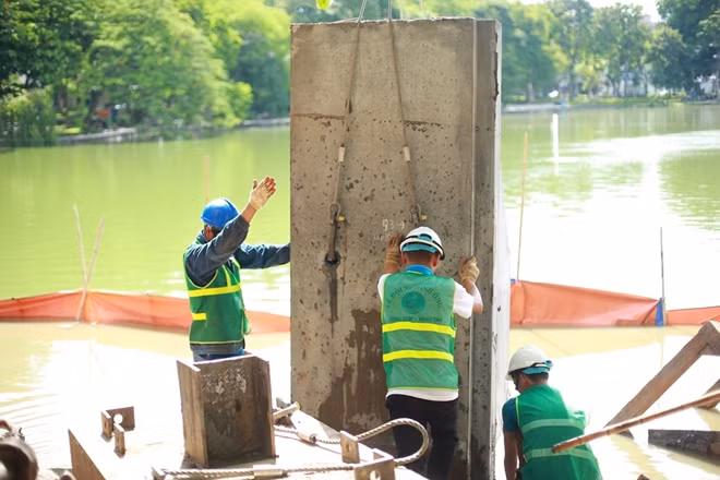 Các công nhân thực hiện dự án kè hồ Gươm đang cố định một khối bê tông vào vị trí.