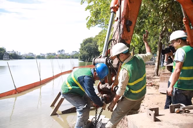 Một máy xúc (đã được tháo gầu) sẽ được sử dụng để cẩu khối cấu kiện trên vào vị trí trên kè.
