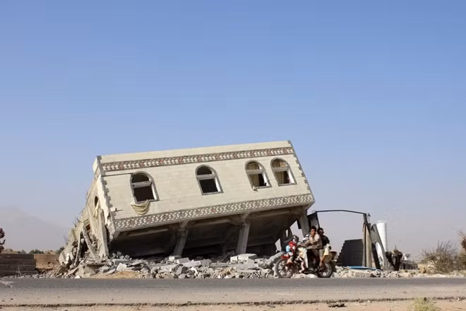 Hai người đàn ông đi qua một tòa nhà sập ở Yemen sau cuộc không kích của Saudi Arabia.