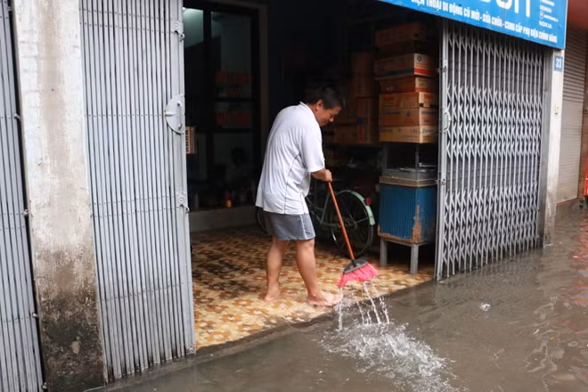 Một người dân trên phố Bùi Xương Trạch đang quét nước ra khỏi nhà sau khi con mưa lớn khiến con phố này ngập nặng.