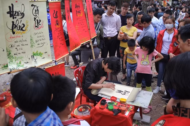 Mọi người xếp hàng vây quanh bàn thư pháp chăm chú theo dõi từng nét bút của “ông đồ” còn khá trẻ.