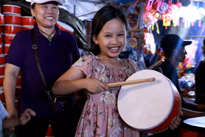 Một cô bé phấn khích với chiếc trống được bố mẹ mua cho khi đi chơi phố vào buổi tối.
