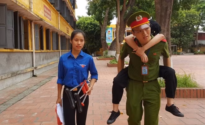 Phan Tuấn Hùng đang cõng thí sinh không may bị tai nạn gãy chân từ phòng thi ra cổng trường. (Ảnh: Lê Văn)