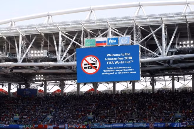 Tấm biểu ngữ to lớn kia cũng không ngăn được Maradona tận hưởng hương vị xì gà. Ảnh: Reuters.