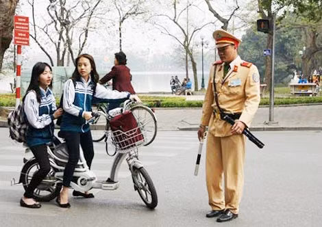 Cán bộ CSGT tuyên truyền học sinh đi xe đạp điện đội mũ bảo hiểm.