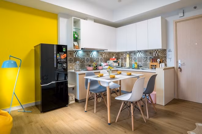 Bếp và bàn ăn được bố trí trong góc cùng hệ tủ màu trắng khiến khu bếp tuy nhỏ nhưng vẫn rất tiện nghi. Căn bếp nhìn khá bắt mắt bởi màu phối hài hòa giữa vàng, hồng và xanh ngọc.