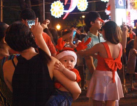 Một em bé ngắm nhìn đèn hoa lung linh khi cùng cha mẹ đón giáng sinh trên đường phố.