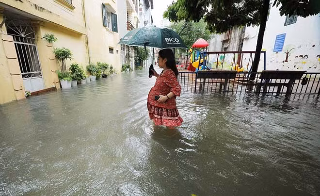 Nước ngập sâu khiến nhiều tuyến phố ngày thường đông đúc người qua lại, nay trở nên vắng vẻ. Ảnh chụp một phụ nữ mang bầu cố gắng lội qua đoạn ngập sâu 40 cm trong con ngõ nhỏ.