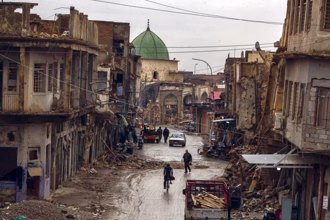 Người dân đi qua trước các tòa nhà bị hư hại ở thành phố cổ Mosul, Iraq, vào tháng 11. Hơn một năm sau khi giao tranh tàn khốc giải phóng thành phố kết thúc, và một chiến dịch không quân tàn khốc chủ yếu san phẳng nó, phần lớn thành phố nằm trong đống đổ nát. (Ảnh: Victor J. Blue)