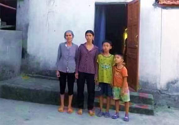 Mẹ, vợ và các con anh Tuyển trước căn nhà dột nát.