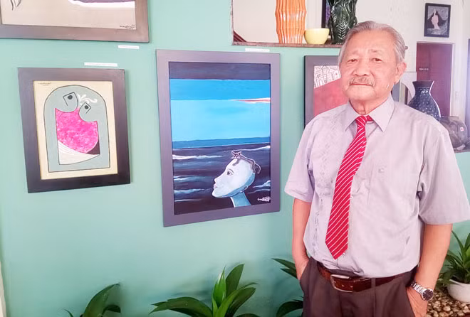 Nhà văn Mường Mán bên các tác phẩm hội họa của mình tại triển lãm “Tuần trăng mê hoặc”.