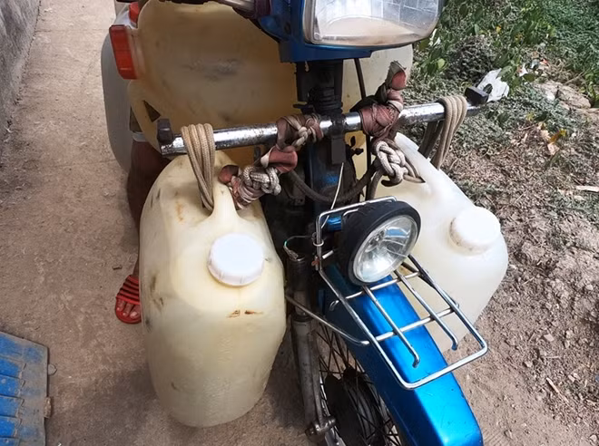 Xe gắn máy được độ thêm càng sắt để chở được nhiều thùng nước.