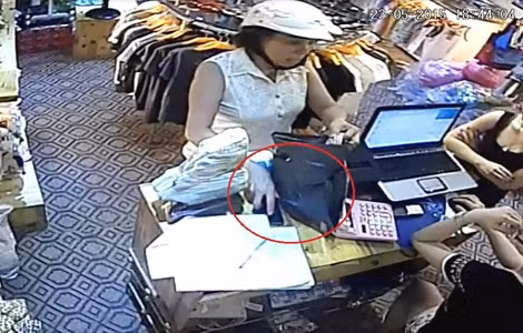 Người phụ nữ nhanh chóng kẹp chiếc điện thoại trên bàn (ảnh cắt từ camera giám sát của shop quần áo). Người phụ nữ nhanh chóng kẹp chiếc điện thoại trên bàn (ảnh cắt từ camera giám sát của shop quần áo).
