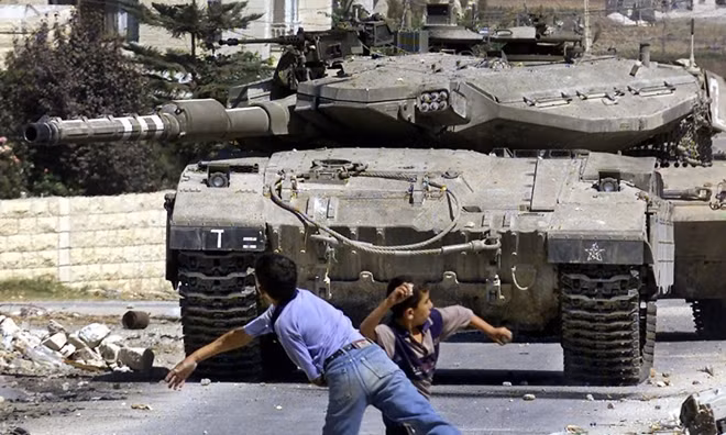 Thanh niên Palestine ném đá vào xe tăng Israel. Ảnh: AP