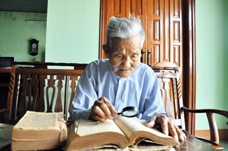 Mắt kính bị hỏng nên cụ Huỳnh Cát phải đọc sách bằng kính lúp.