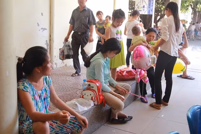 Hành lang và phòng chờ chật kín chỗ, người nhà bệnh nhi phải ra ngoài ngồi dưới những bóng râm.