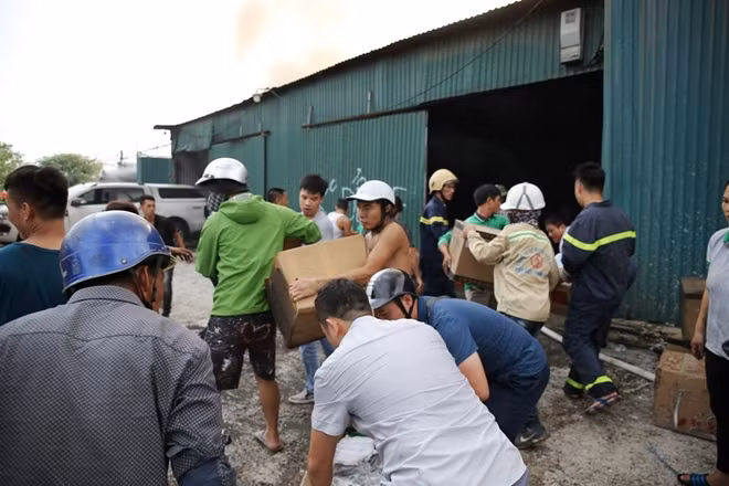 Cảnh sát đã có mặt tại hiện trường và huy động người dân hỗ trợ di chuyển nhiều thùng hàng từ bên trong nhà xưởng ra ngoài.