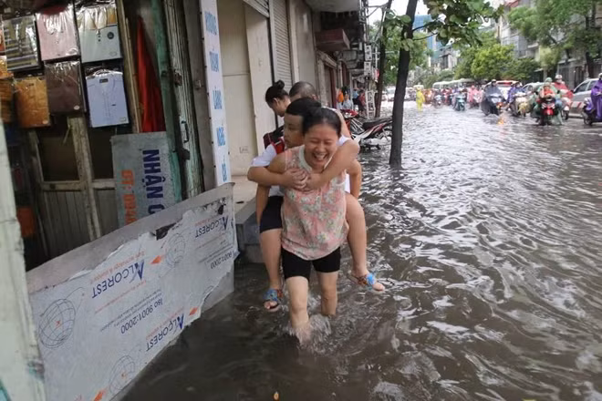 Các em học sinh nhỏ được người lớn trong gia đình cõng đến khu vực cao hơn không bị ngập để đưa đến lớp.