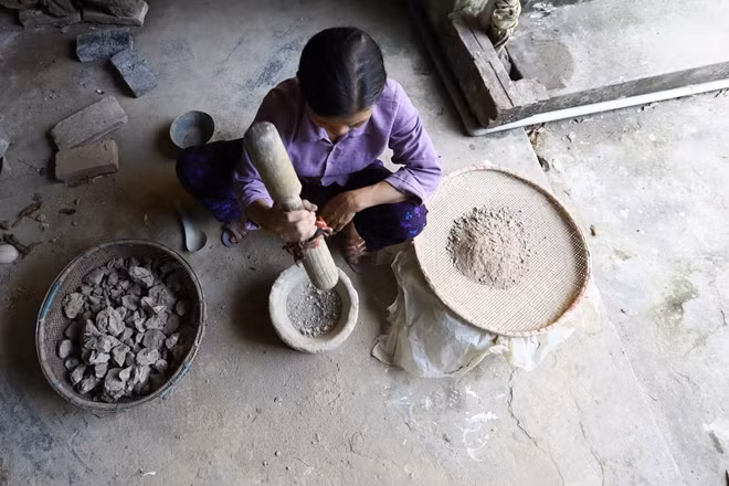 Bà Điểu - vợ ông Giáp giã đất thó rồi sàng lấy bột mịn như bột mỳ. Đất thó hay còn gọi là đất sét được đào ngoài đồng rồi mang về phơi khô, nhìn như cục đá.