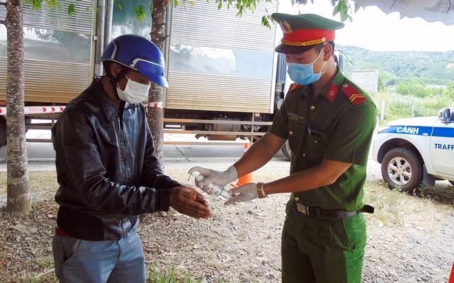 Chiến sĩ Công an hỗ trợ người dân rửa tay sát khuẩn tại chốt kiểm soát dịch COVID-19 khu vực đèo Lò Xo, xã Phước Mỹ, huyện Phước Sơn.