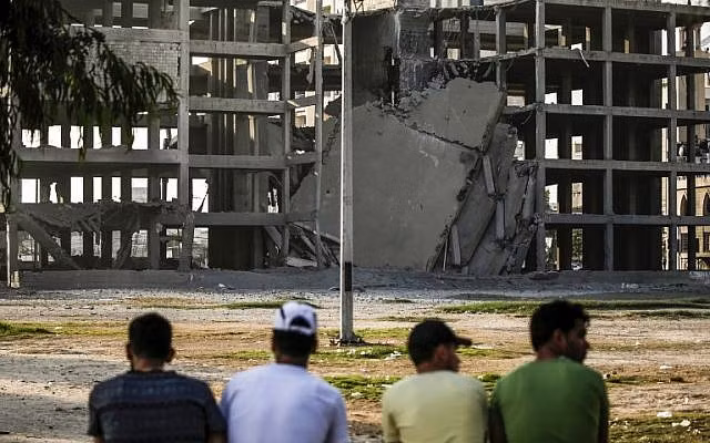 Một nhóm thanh niên Palestine ngồi nhìn tòa nhà từng được Hamas dùng làm cơ sở huấn luyện vũ trang bị Israel phá hủy hôm 14-7. Ảnh: AFP
