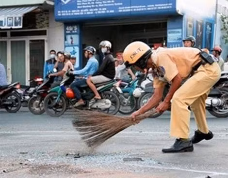 Sau vụ TNGT tại Hóc Môn, một CSGT lấy chổi quét dọn những mảnh kính vỡ nát trên đường.