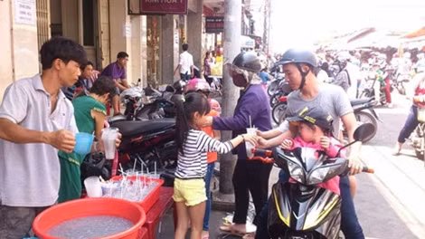 Một em bé theo cha ra chợ phát nước hột é miễn phí cho khách hành hương ở chùa Bà.