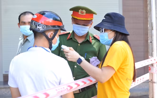 Cán bộ và lực lượng Công an phường đo thân nhiệt, hướng dẫn người dân trong khu vực phong tỏa