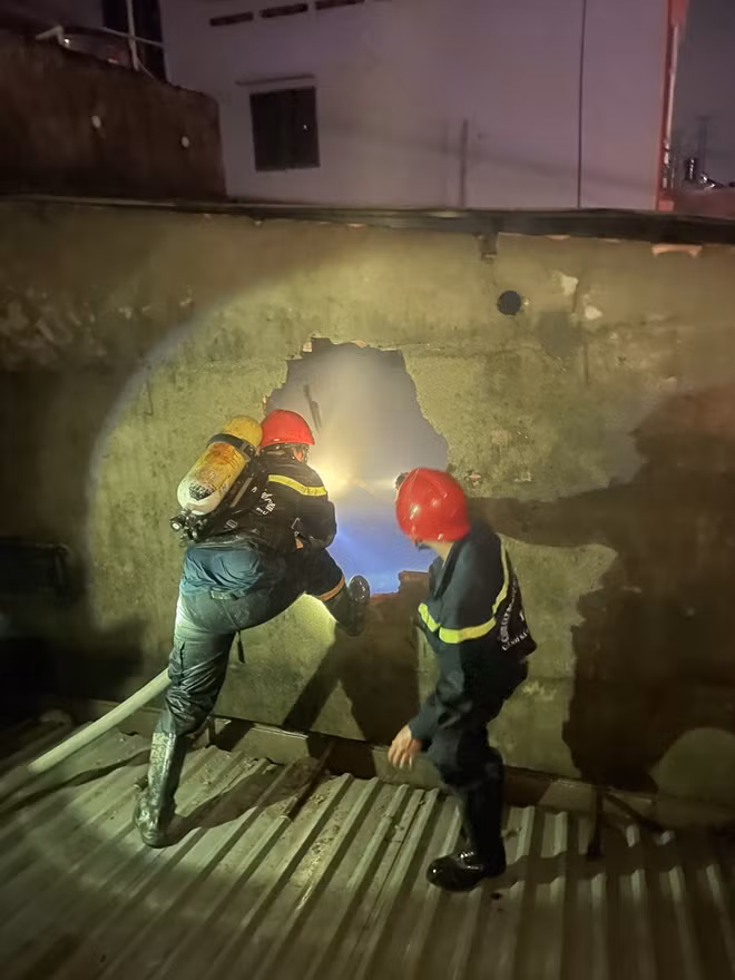 Cán bộ chiến sĩ PCCC phá tường để đưa 3 nạn nhân trong vụ cháy ra ngoài.