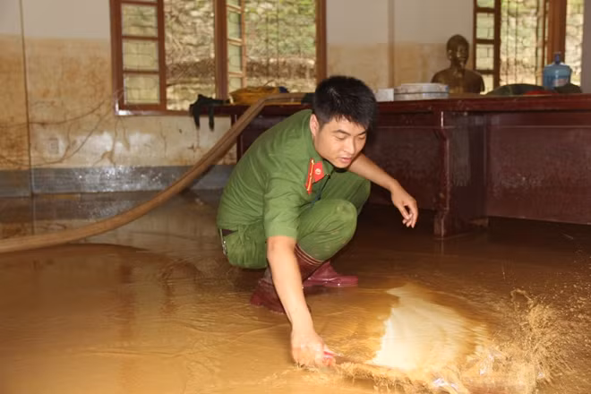 Cán bộ công an đồn Nà Ớt dùng chổi đẩy bùn và nước trong phòng học