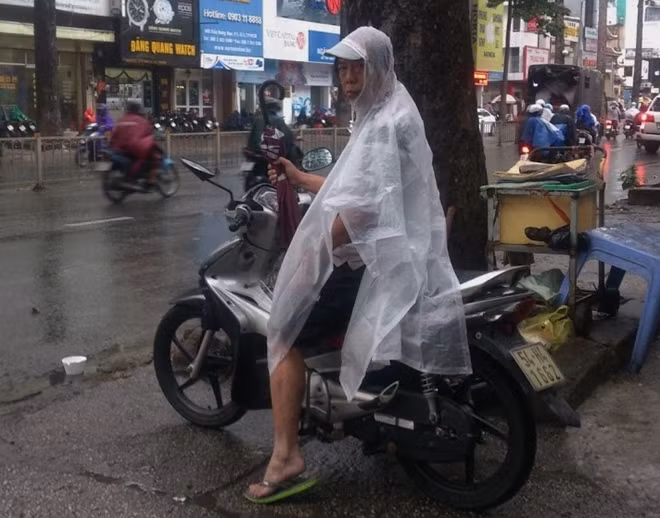Một người đàn ông cẩn thận mặc áo mưa và mang theo dù khi ra đường