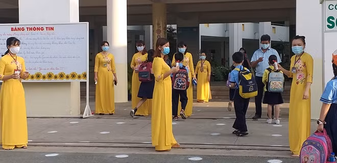 Giáo viên và nhân viên Trường Tiểu học Nguyễn Hiền (quận 2) đo thân nhiệt và hướng dẫn HS rửa tay khử khuẩn tại cổng trường