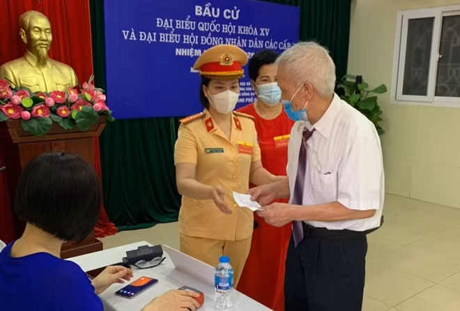 Nữ cán bộ Đội CSGT trật tự Công an quận Đống Đa hướng dẫn cử tri cao tuổi quy định về bầu cử.