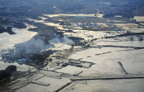 Khói bốc lên từ một khu vực bị ngập lụt sau trận sóng thần tại Fukushima.