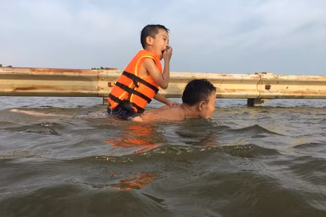 Một em nhỏ được bố kiệu sau lưng đùa nghịch trong nước.