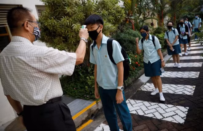 Học sinh xếp hàng với khoảng cách 1m để đo thân nhiệt trước khi vào lớp. Ảnh: Reuters