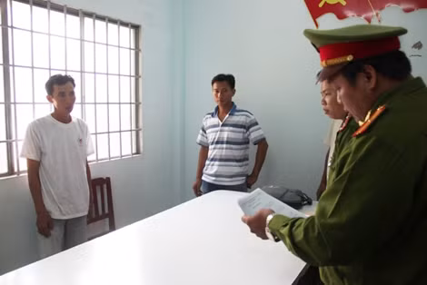 Cơ quan điều tra đọc lệnh bắt đối với Trần Quốc Gia, áo trắng đứng bên trái.