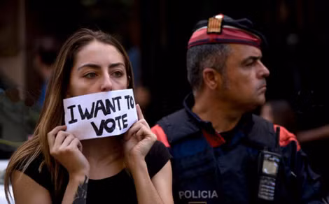 Một phụ nữ Catalonia đứng cạnh một cảnh sát Tây Ban Nha với khẩu hiệu “Tôi muốn bầu cử”.