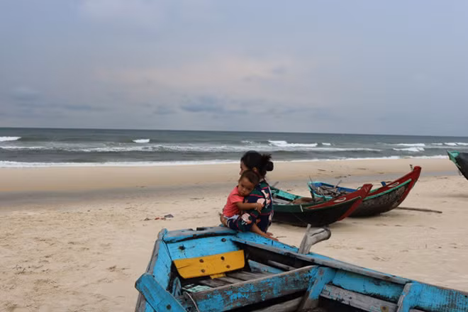 Trên bờ biển Hải Ninh, chị bồng con với tâm trạng lo lắng chờ chồng trên biển mau vào đất liền tránh bão.