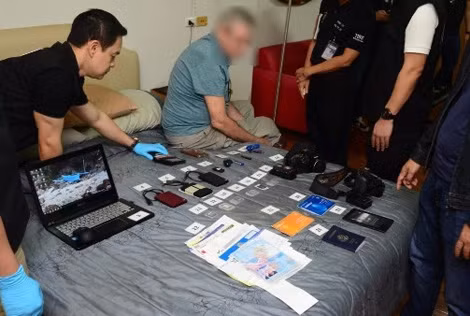 Nhân viên TICAC khám xét máy tính của Douglas Wayne Canete, 68 tuổi, người Mỹ (ngồi giữa) ở Chiang Mai - bị buộc tội sở hữu hình ảnh khiêu dâm trẻ em. Nhân viên TICAC khám xét máy tính của Douglas Wayne Canete, 68 tuổi, người Mỹ (ngồi giữa) ở Chiang Mai - bị buộc tội sở hữu hình ảnh khiêu dâm trẻ em.