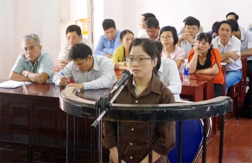Bị cáo Huỳnh Nguyễn Quế Trâm đứng trước vành móng ngựa (ông Trần Văn Gôm ngồi bìa trái, tiếp đến là ông Phạm Lê Kiên, bà Đặng Thị Mỹ Lợi mặc áo màu cam ngồi ngay phía sau bị cáo).