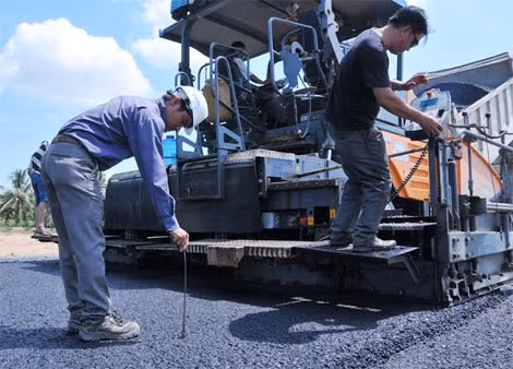 Kĩ sư giám sát công trình đang kiểm tra độ nóng khi trải thảm nhựa trên đường dẫn lên cầu.