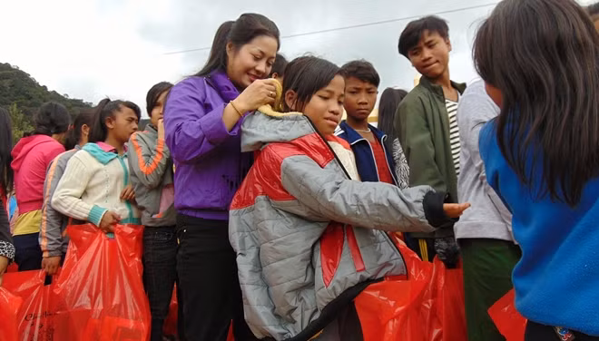 Đại diện Nhóm từ thiện Từ Tâm mặc áo ấm mới cho các em học sinh.