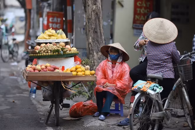 Ngồi bên xe hàng hoa quả trong cái lạnh sớm mùa Đông, cô bán hàng phải mặc thêm áo mưa để giữ ấm cơ thể.