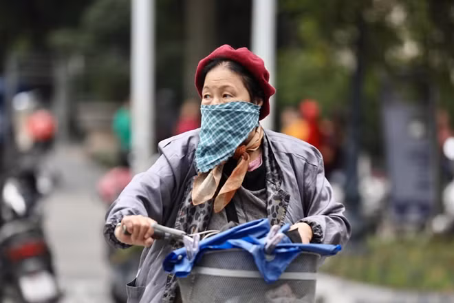 Bác gái trung niên với áo ấm, khăn quàng đạp xe bên hồ Gươm.