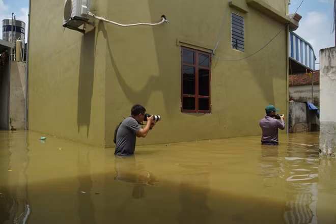 Hai phóng viên Phong Sơn, Chiến Thắng Báo CAND ngâm mình tác nghiệp giữa biển nước ở Chương Mỹ. Theo PV Chiến Thắng, chiếc máy ảnh anh mang theo trị giá cả ống kính hơn 100 triệu đồng. Chính vì vậy, khi tác nghiệp các anh phải bọc ny lon cẩn thận. Đến địa điểm cần "nổ súng", PV phải lần dò kỹ càng địa hình, địa vật dưới nước, sau đó mới cẩn thận dám mang máy ảnh ra sử dụng.