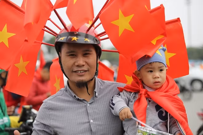 Một CĐV đưa theo con nhỏ tới sân Mỹ Đình, anh chọn cho mình cách thể hiện tình yêu với đội tuyển bằng chiếc MBH cùng chi chít cờ Tổ quốc trên đầu.