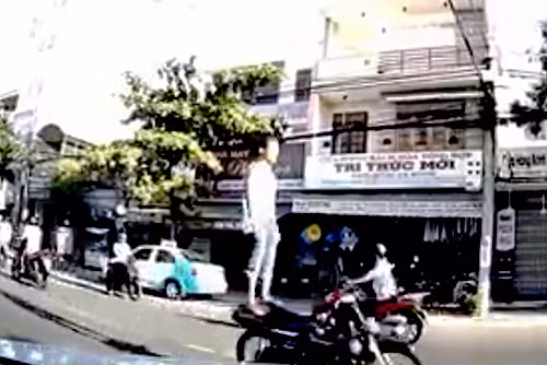 Cảnh một nam thanh niên không đội mũ bảo hiểm, buông 2 tay đứng trên yên xe máy và dùng chân điều khiển giữa tuyến đường đông đúc. Ảnh cắt từ clip